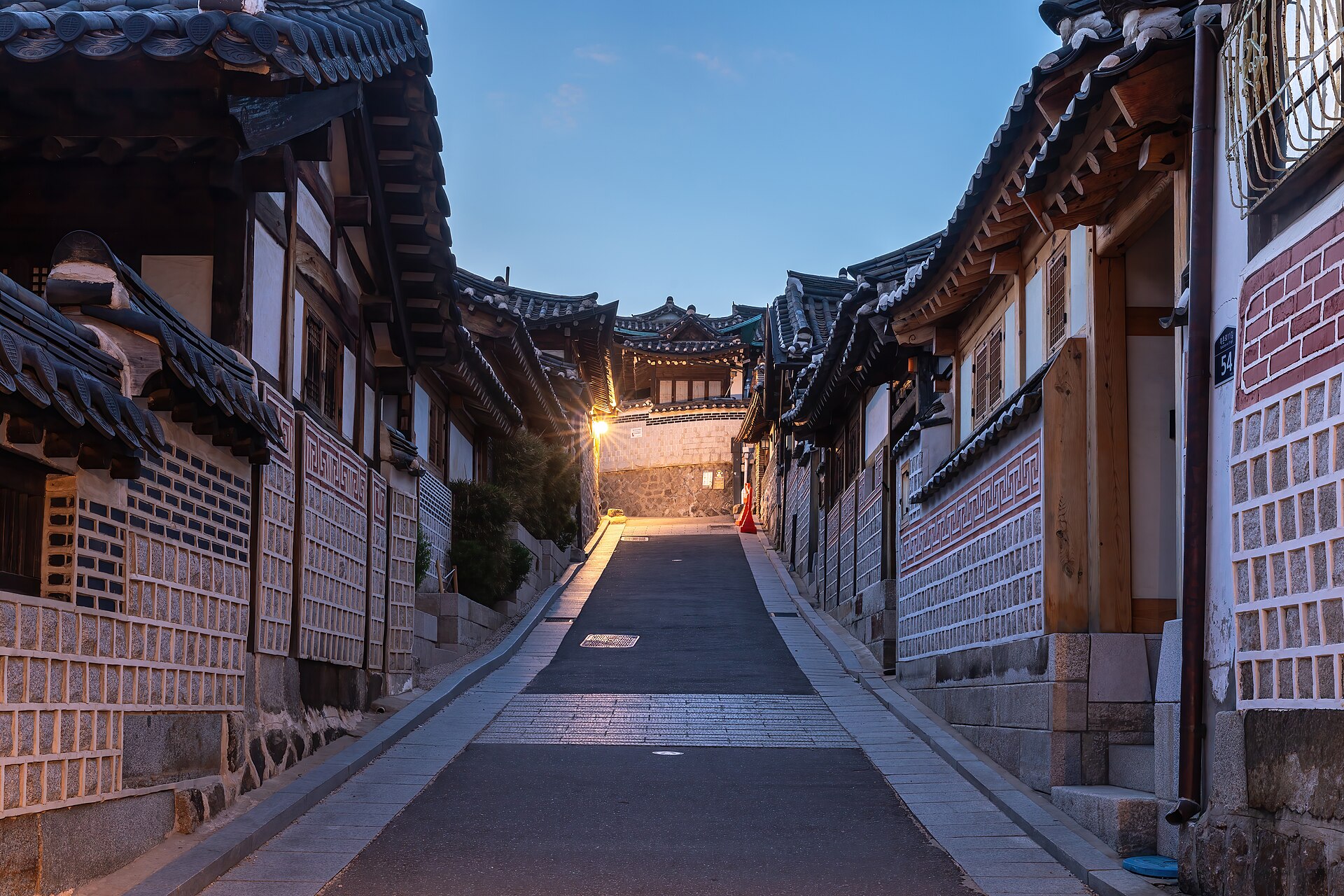 北村韩屋村夜幕蓝调时分，传统瓦顶韩屋沿坡地排列，黑灰色屋脊与暖黄灯光交映