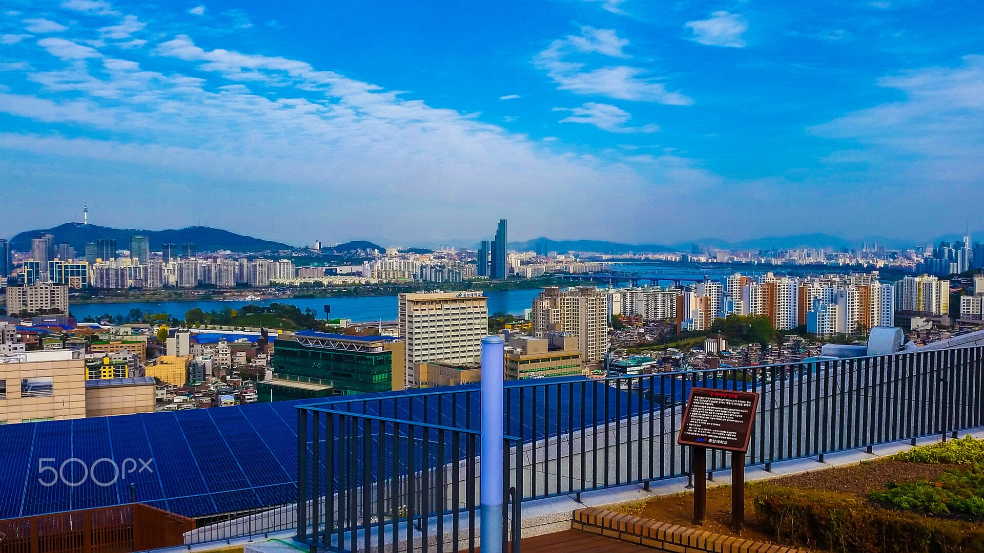 首尔现代天际线与云层交错，城市建筑群密集排列，远处山脉若隐若现